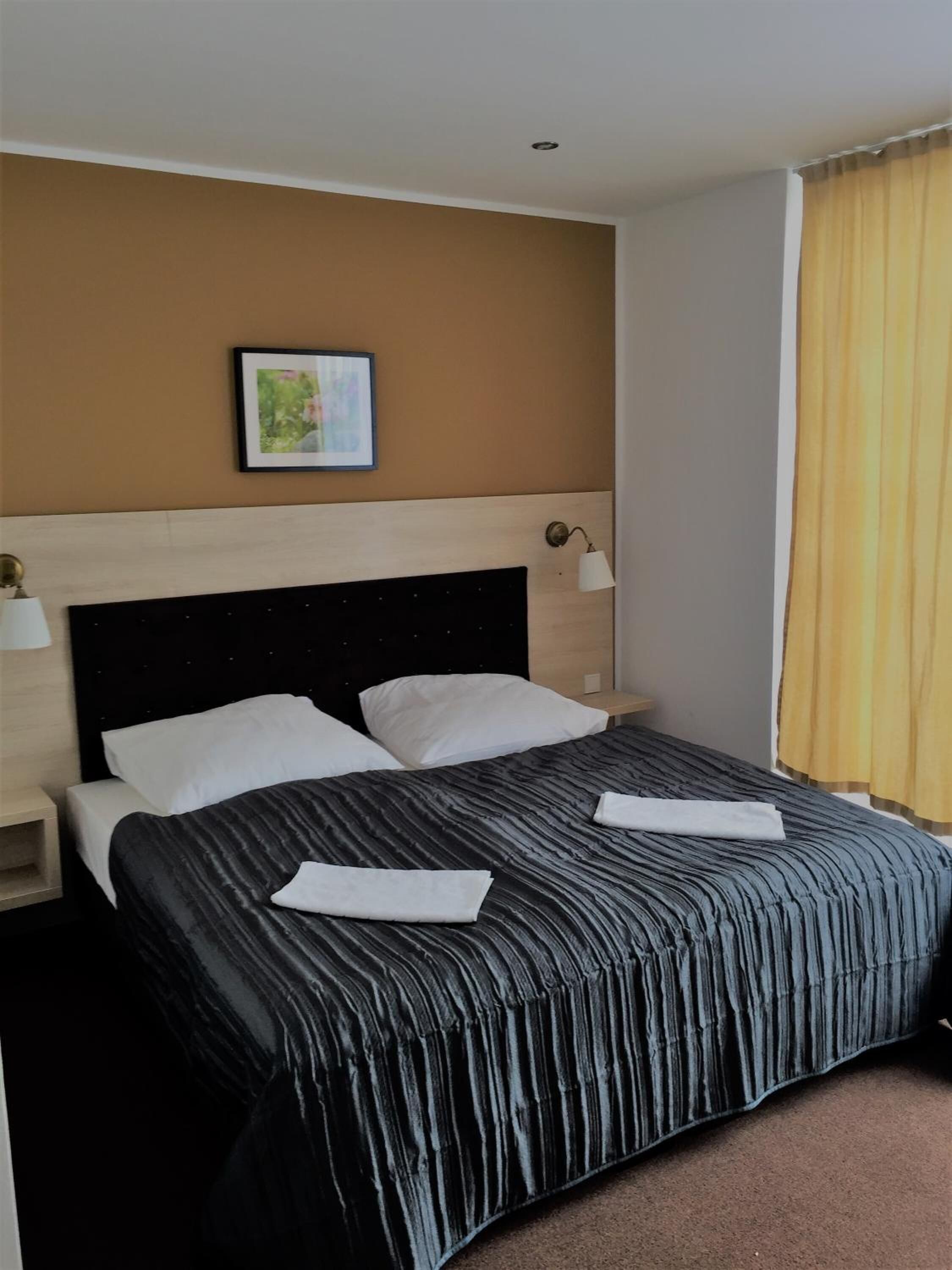 Quarto de hotel com cama, duas mesas de cabeceira, um quadro na parede e janela com cortinas.