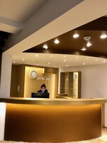 Una recepción de hotel con una recepcionista, un reloj y un letrero que dice "HOTEL DENBU".