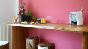 Una mesa de madera con una pared rosa de fondo, un florero con flores, dos vasos de jugo de naranja y una botella de champán.