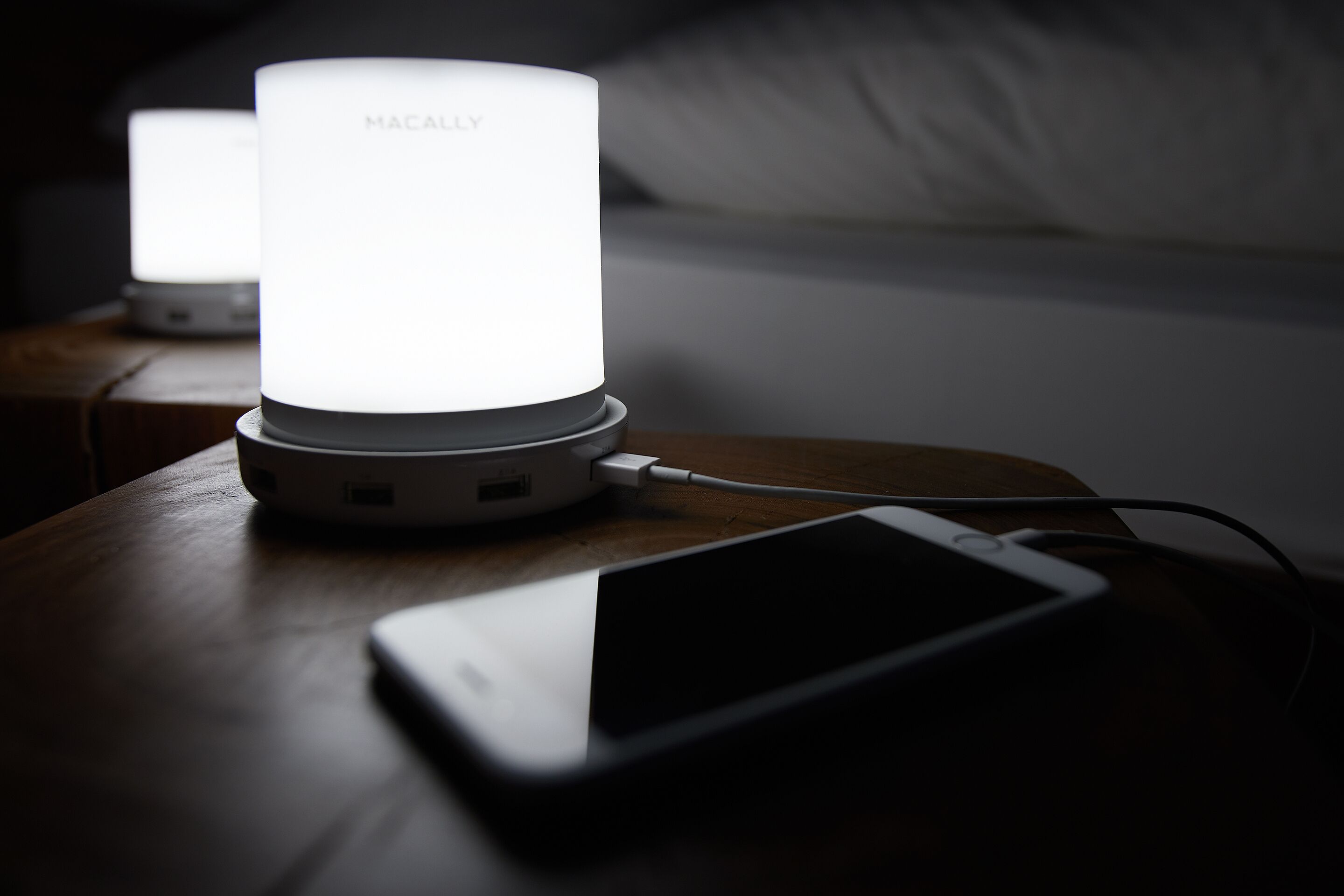 A MacBook on a wooden table with a white Mac mini and a smartphone connected to it.