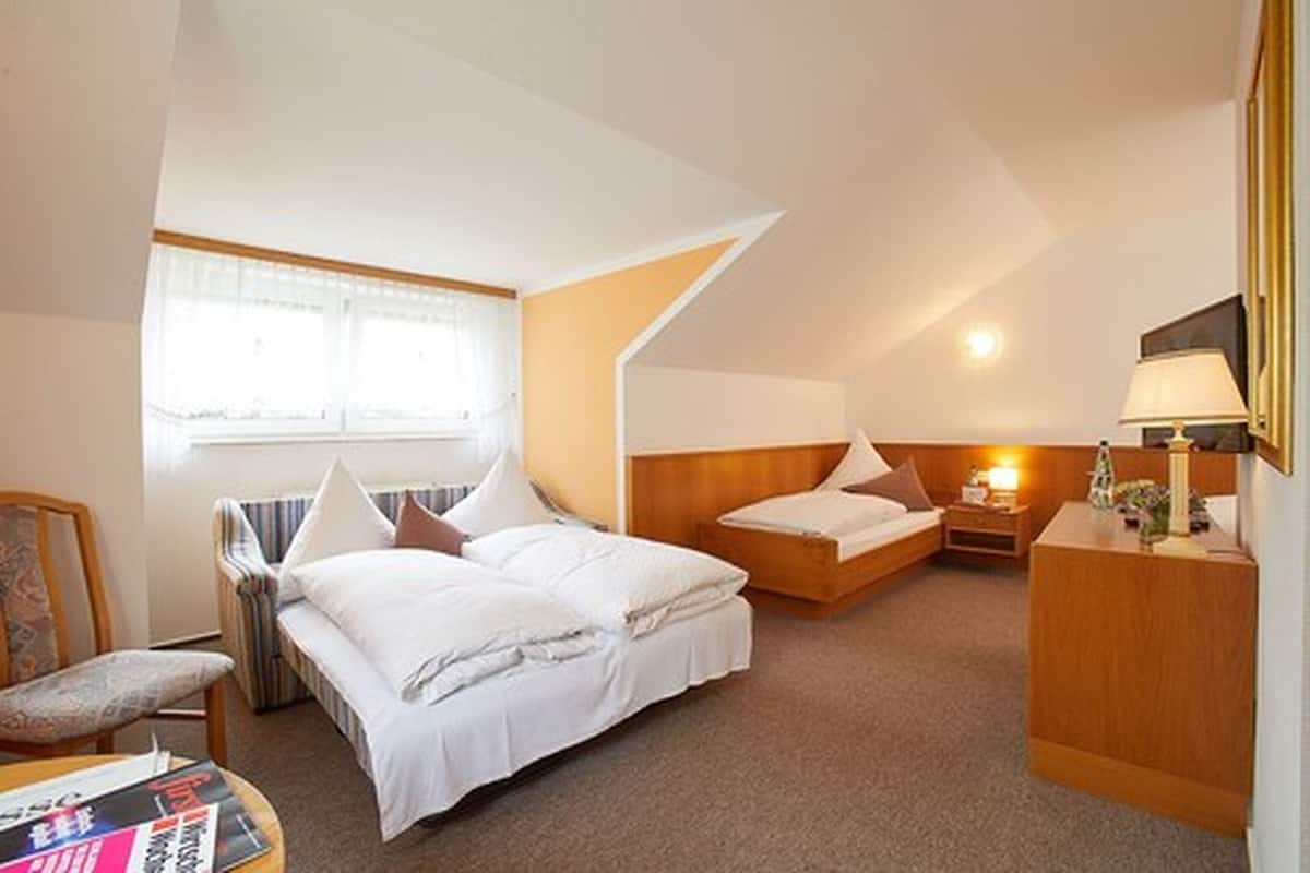 A hotel room with two beds, a desk, a chair, and a window.