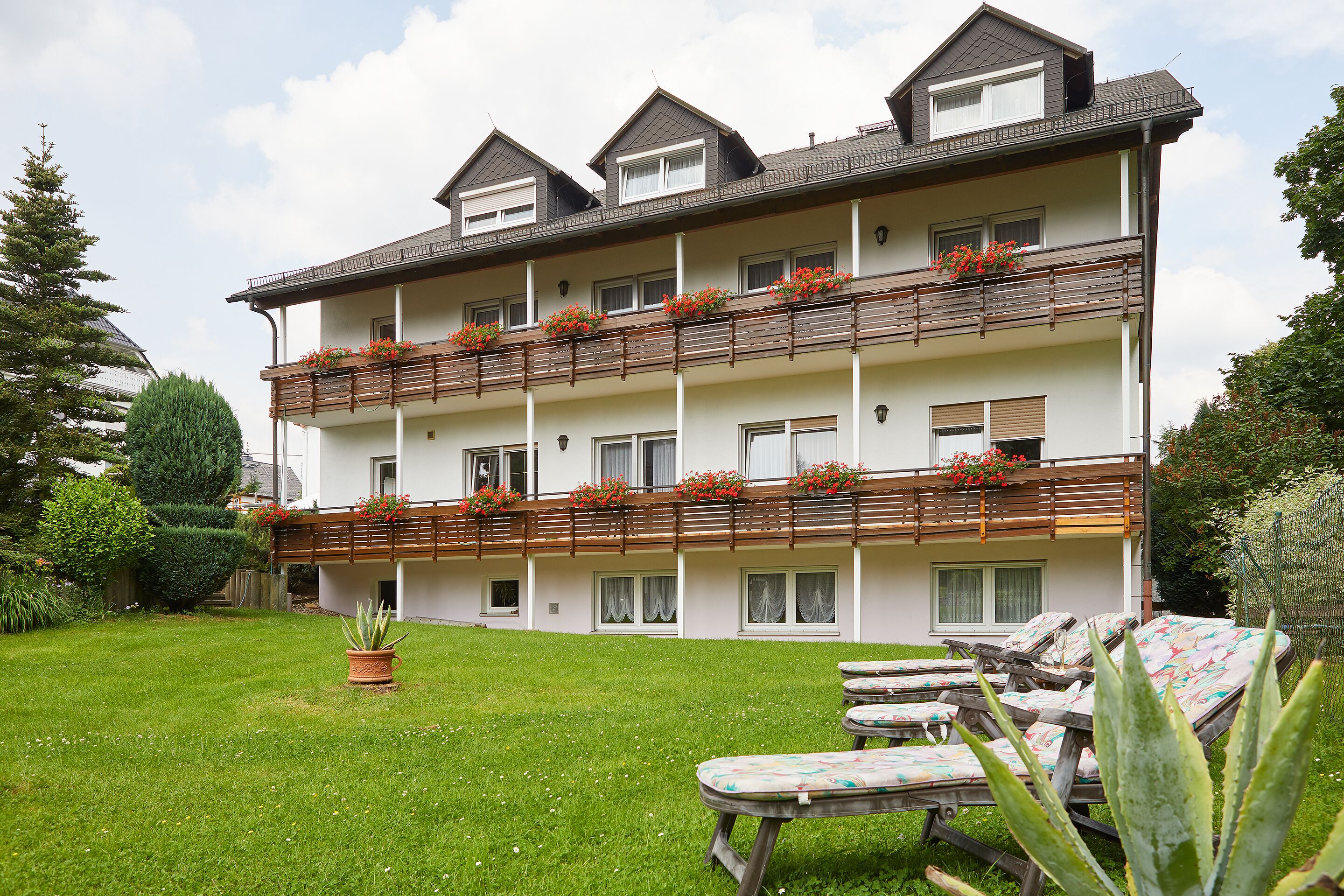 Un hotel de varios pisos con balcones, un césped cuidado y mobiliario exterior.