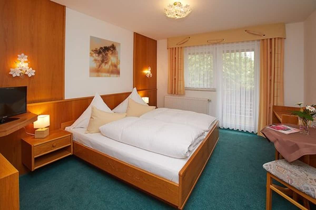 A neatly arranged bedroom with a bed, bedside tables, a television, and a window with curtains.