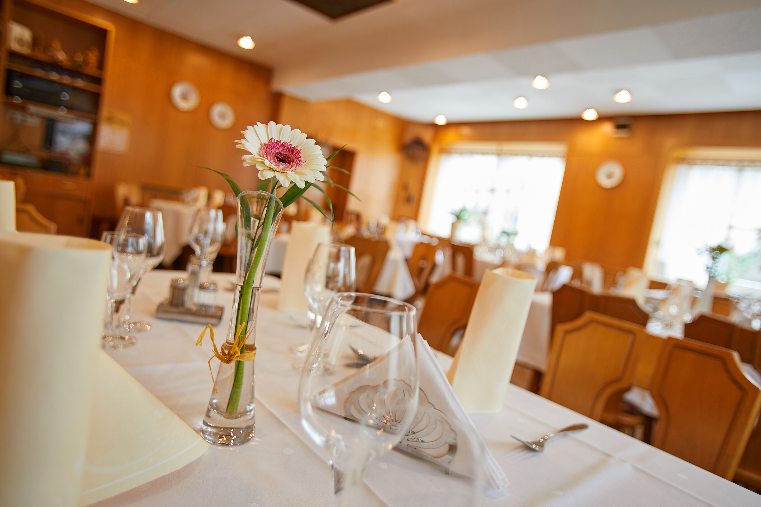 A dining table set with wine glasses, a vase with a flower, and a napkin.