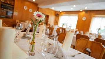 A dining table set with wine glasses, a vase with a flower, and a napkin.