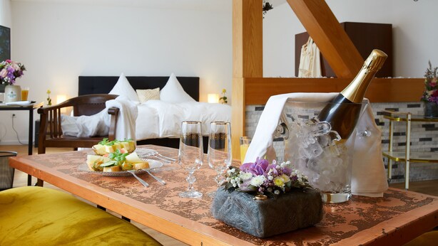 Habitación de hotel con cama, una mesa de comedor, una botella de champán, copas y un arreglo floral.