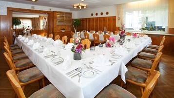 A dining area with a long table set for a meal, wooden chairs, and a wooden panel wall.
