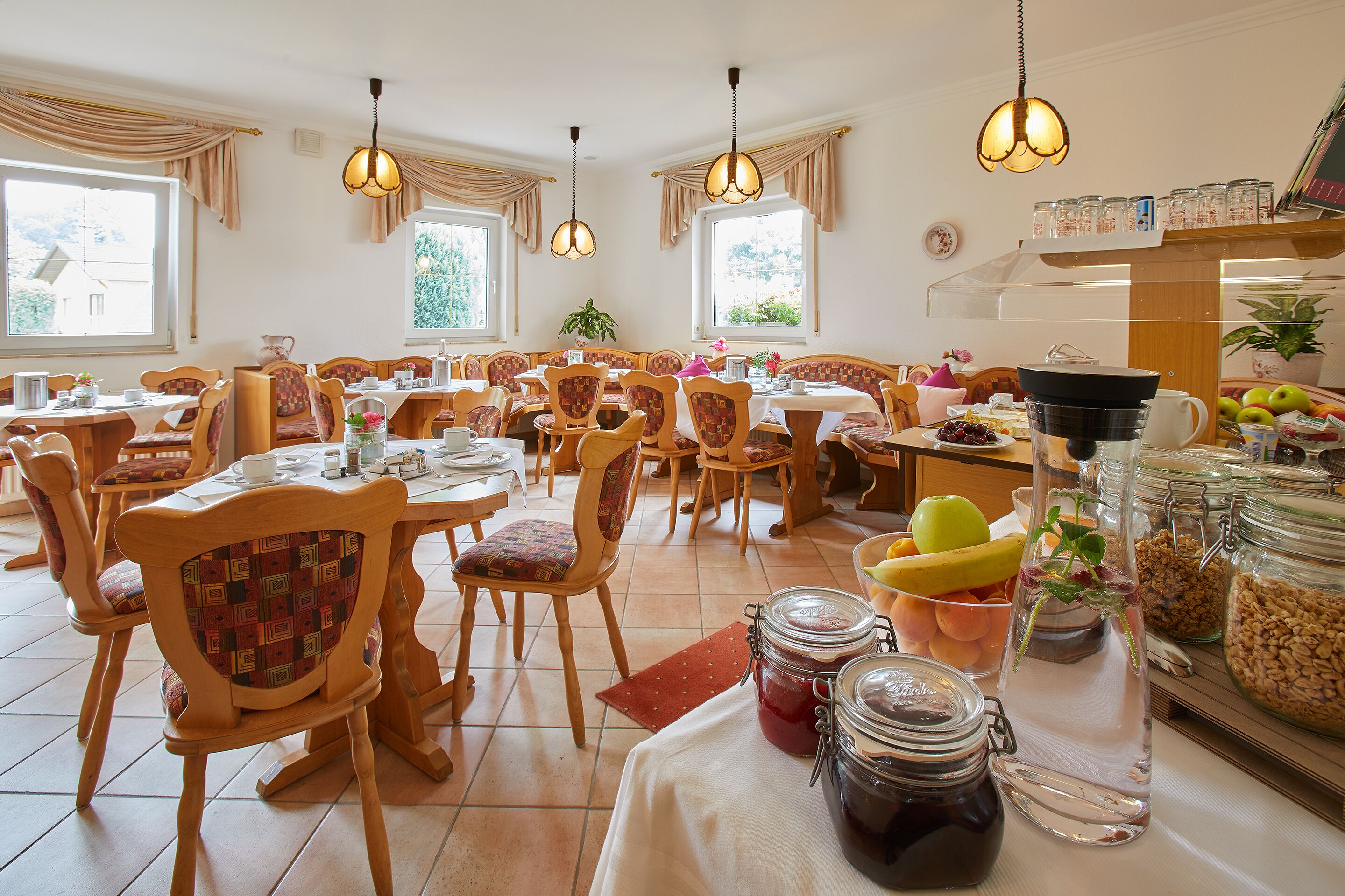 Un espace repas avec plusieurs tables et chaises, un buffet proposant divers plats, et des lampes suspendues décoratives.