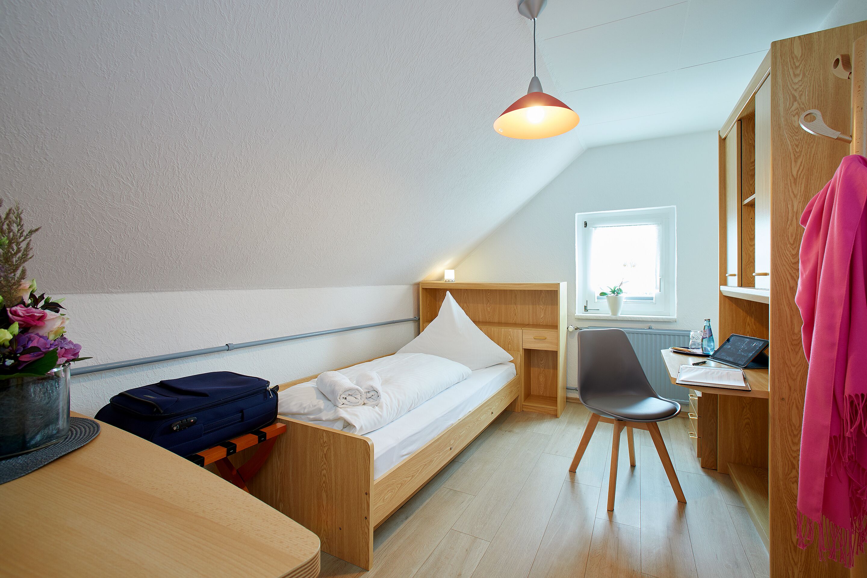 Una habitación compacta con una cama individual, un escritorio, una silla y una lámpara colgante.