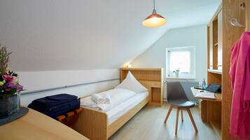 Una habitación compacta con una cama individual, un escritorio, una silla y una lámpara colgante.