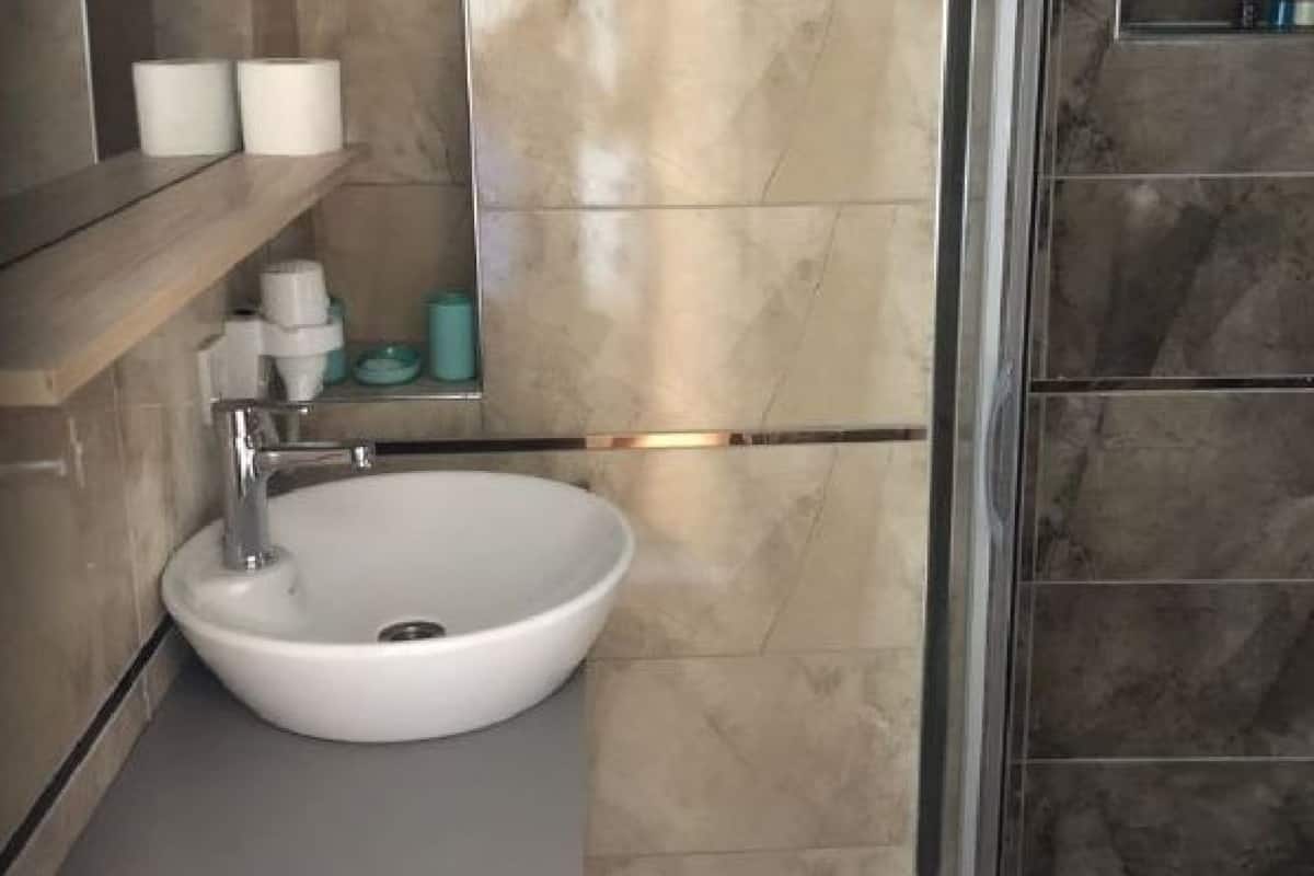 Ein Badezimmer mit einem weißen Waschbecken, einem Spiegel und einem Ablagebereich für Toilettenartikel.
