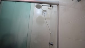 Chuveiro com chuveiro manual, comando fixado na parede e porta com painel de vidro fosco.