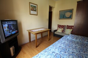 A room with a TV on a stand, a wooden table, a sofa with patterned cushions, and a bed with a blue patterned bedspread. - Go house Arouche SP 804 (São Paulo)