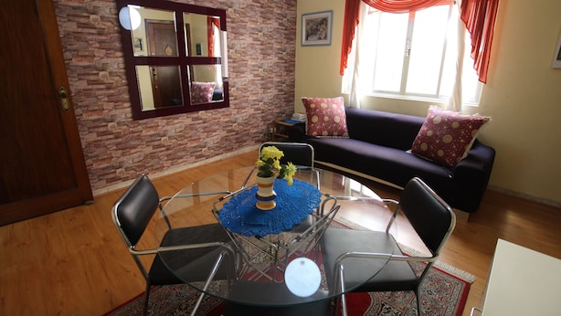 Uma sala de estar com uma mesa de vidro, cadeiras, um sofá e uma parede de tijolos.