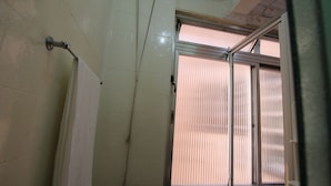 Casa de banho com chuveiro, porta-toalhas e janela com estores.