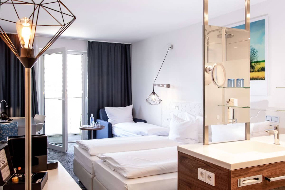 A hotel room with a bed, bedside table, lamp, and a bathroom with a mirror and sink.