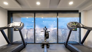 A gym with two treadmills, a central elliptical machine, and a large window offering a city view. - Dorint Hotel Düren (Dueren)