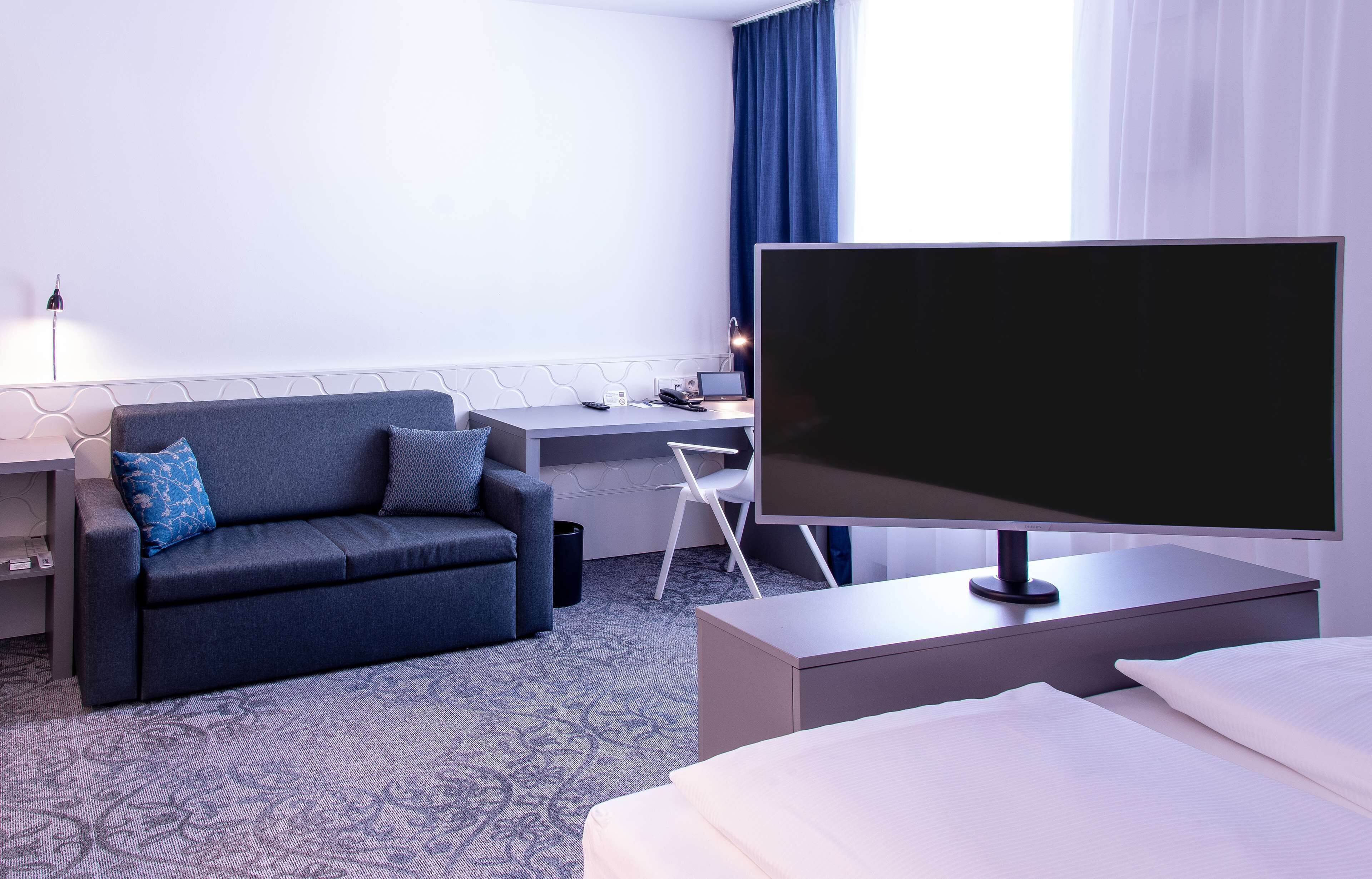 A hotel room with a bed, a desk with a computer, a couch, and a TV.