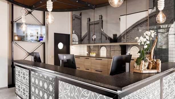 A modern bar area with a counter, seating, and decorative elements like a plant and a unique light fixture. - Dorint Hotel Düren (Dueren)