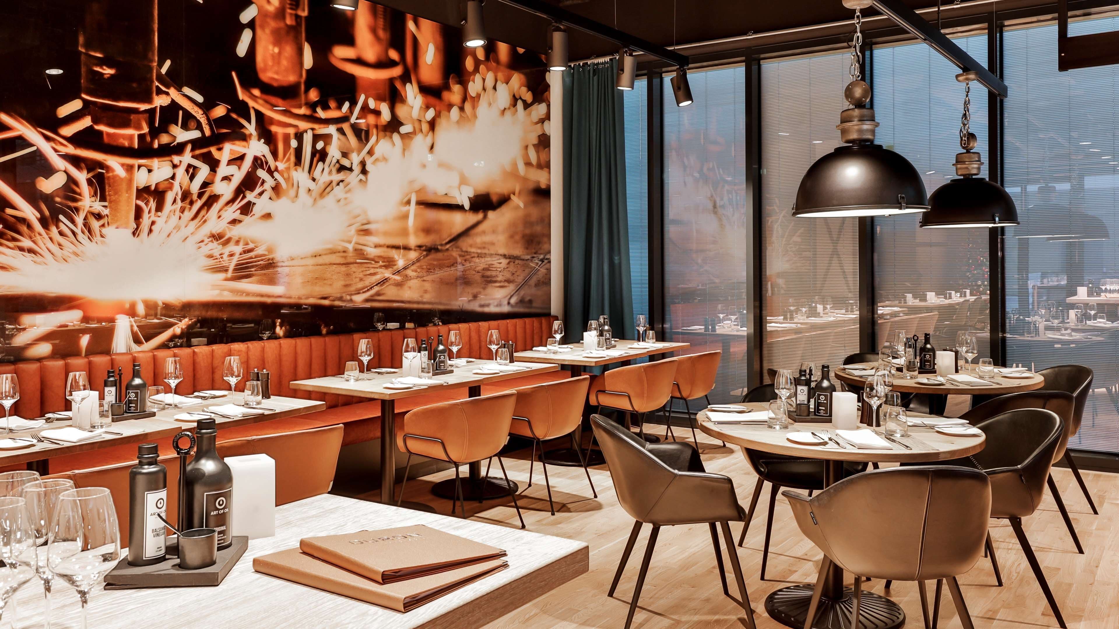 Un restaurante moderno con techo alto, amplios ventanales y vista a la ciudad. Las mesas están dispuestas con copas de vino, botellas y menús.
