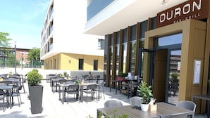 An outdoor seating area with tables and chairs, a potted plant, and a sign for Duron Bar & Grill. - Dorint Hotel Düren (Dueren)