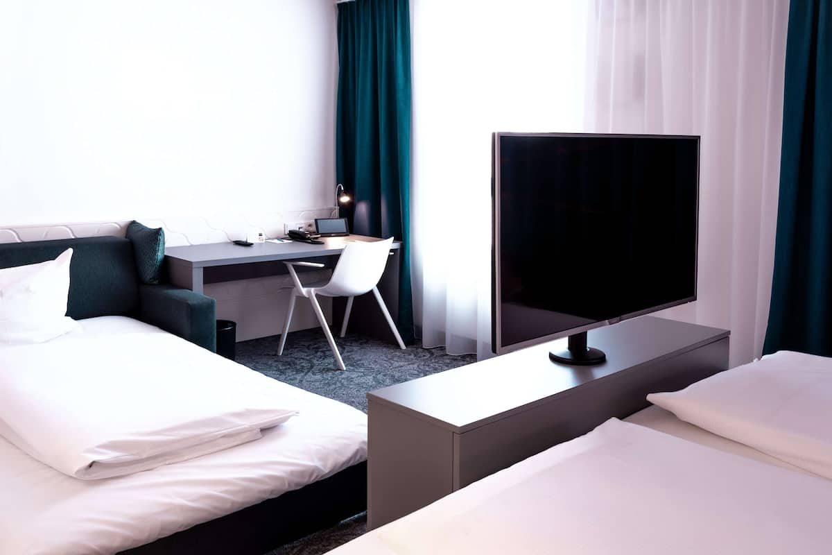 A hotel room with two beds, a desk with a computer, and a TV.