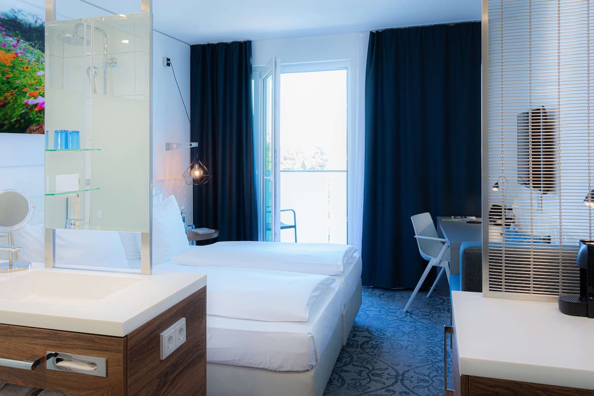 A hotel room with a bed, a desk, a chair, a bathroom with a mirror, and a window with curtains.