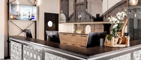 A reception area with a modern design, featuring a patterned tile wall, a wooden reception desk, and hanging light fixtures.