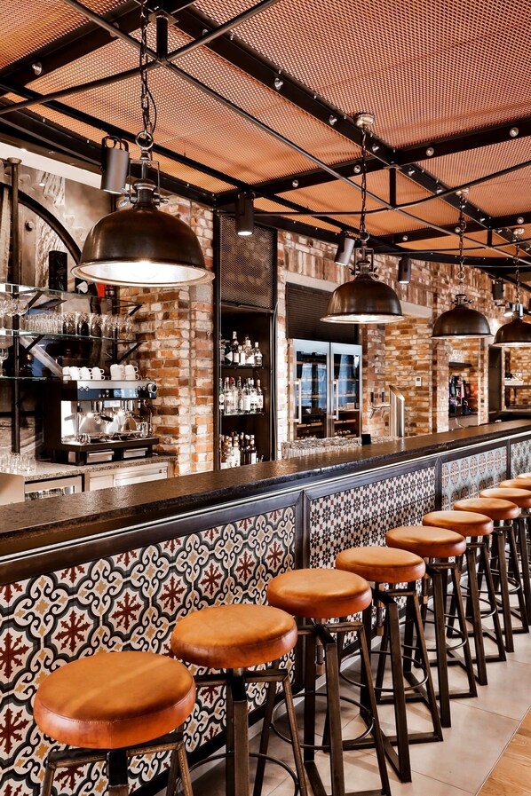 A bar area with a long counter, multiple stools, and hanging lights.