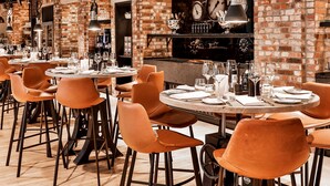 A restaurant with brick walls, round tables, and orange chairs. - Dorint Hotel Düren (Dueren)