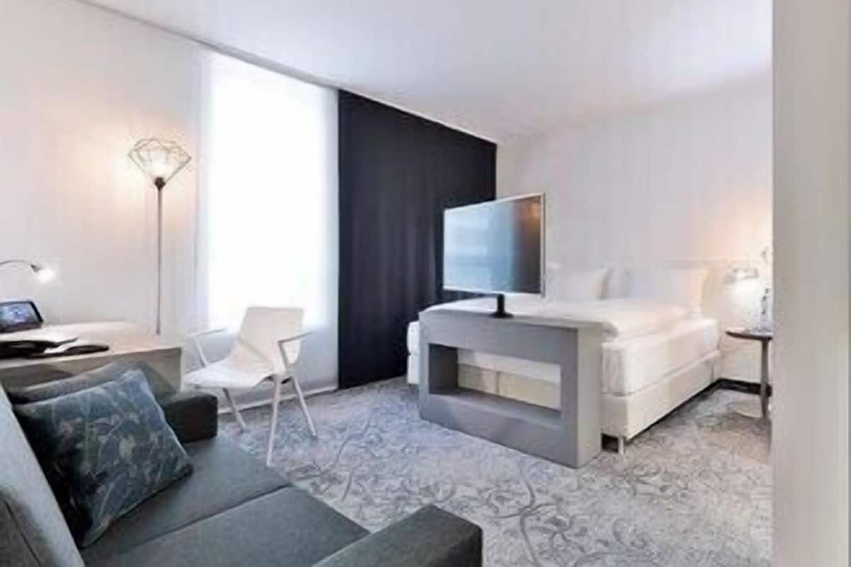 A modern hotel room with a sofa, a TV, a desk, and a chair.