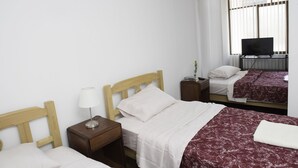 Ein Hotelzimmer mit zwei Betten, einem Fernseher und einem Fenster mit Jalousien.