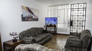 Ein Wohnzimmer mit einer Couch, einem Fernseher und einer Topfpflanze.