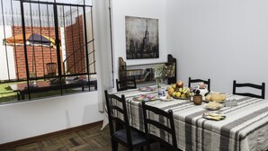 Ein Essbereich mit einem Tisch für vier Personen, umgeben von Stühlen. Ein Fenster mit Blick auf eine Backsteinmauer und eine Tür ist sichtbar.