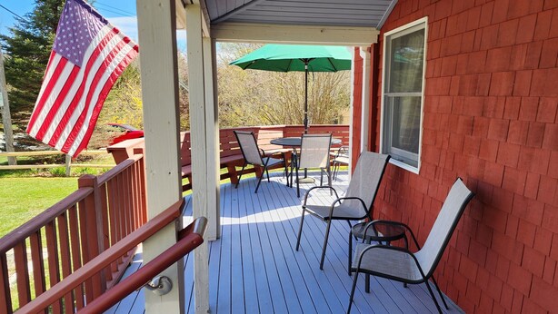 A covered outdoor deck with a table and chairs, an American flag, and a green umbrella.