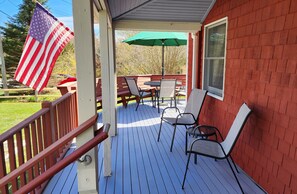 A covered outdoor deck with a table and chairs, an American flag, and a green umbrella.