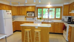A kitchen with wooden cabinets, a white refrigerator, a microwave, a sink, and two stools.