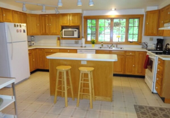 A kitchen with wooden cabinets, a white refrigerator, a microwave, a sink, and two stools.