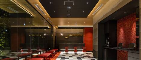 A modern interior with a checkered floor, red benches, and a reception area with a brick wall.