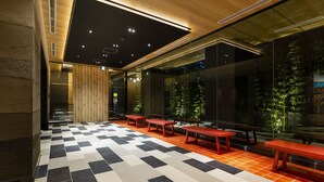 A modern interior with checkered flooring, red benches, and a glass wall with greenery. - the b asakusa (Tokyo)
