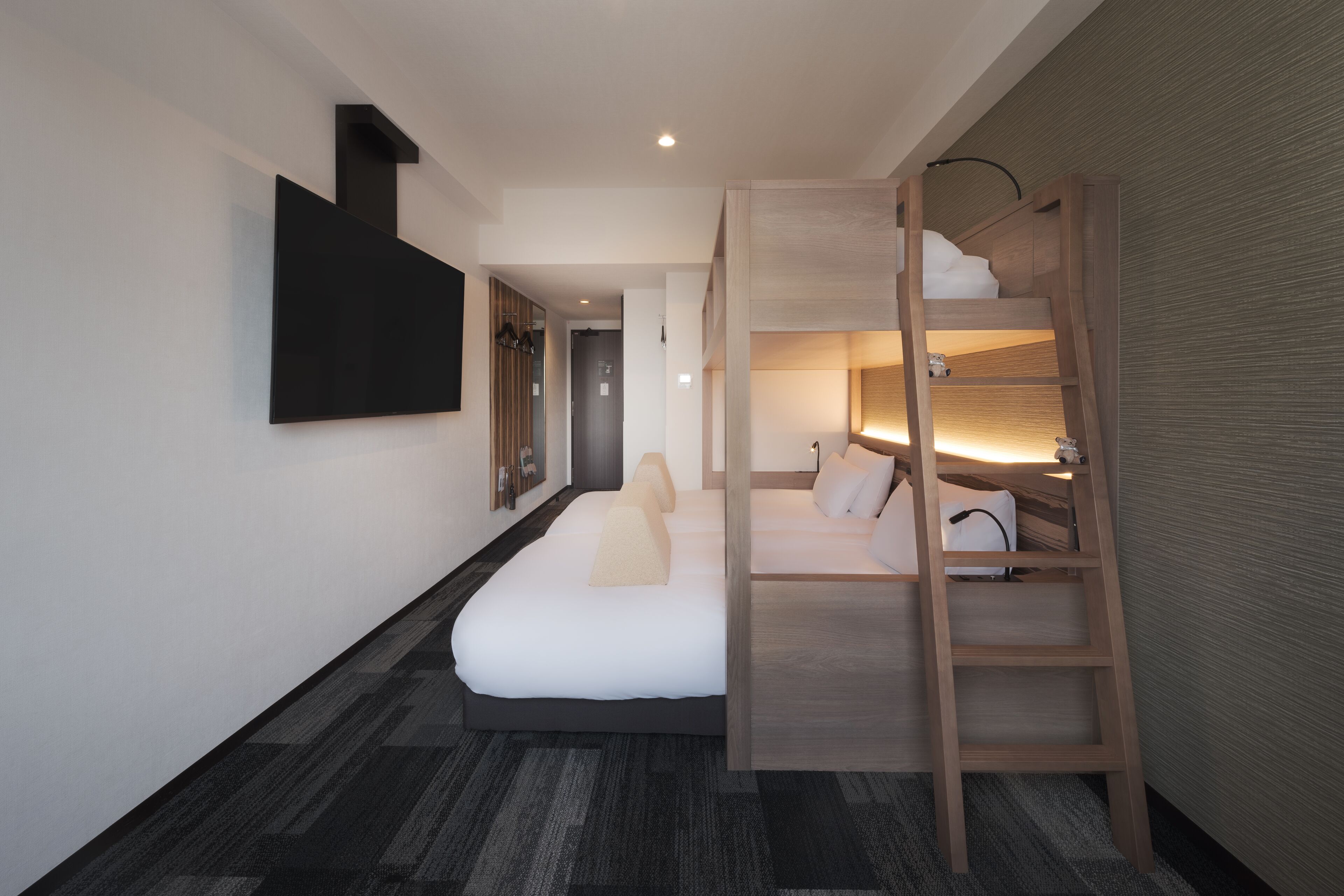 Une chambre d’hôtel moderne équipée d’un lit superposé, d’un téléviseur à écran plat fixé au mur et d’une échelle en bois.