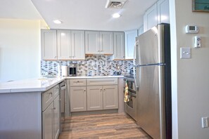 A modern kitchen with light grey cabinets, a stainless steel refrigerator, and a patterned backsplash.