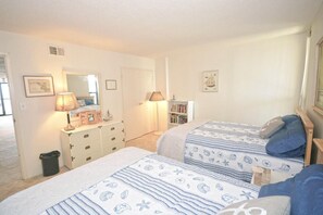 A bedroom with two beds, a dresser, a lamp, a bookshelf, and a door.