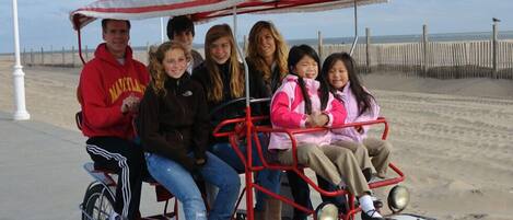 A group of people on a red and white beach buggy with a canopy, parked on a sandy beach with a wooden fence in the background.