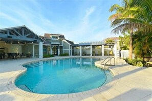 A swimming pool with a curved edge, surrounded by a patio area with chairs and tables.