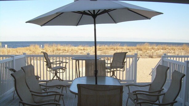 A deck with a table and chairs, an umbrella, and a view of the beach and ocean. - Ocean Colony 11, direct ocean front townhouse at 47th street (Ocean City)