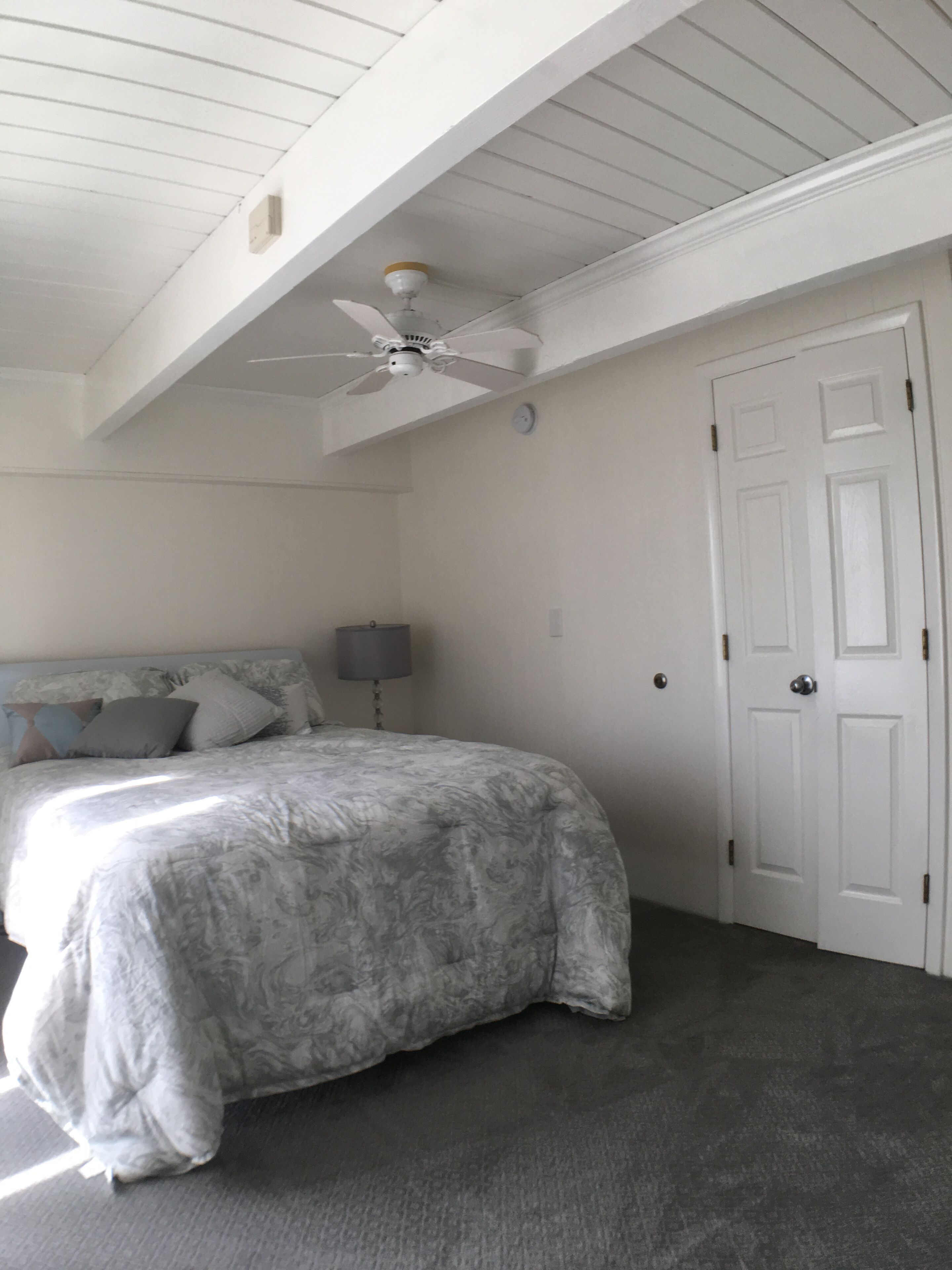 Een slaapkamer met een bed, plafondventilator, deur en lamp.