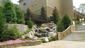 A stone pathway leading to a building with a stone wall and a small waterfall.