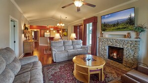 A living room with a stone fireplace, a ceiling fan, and a large TV mounted above it.