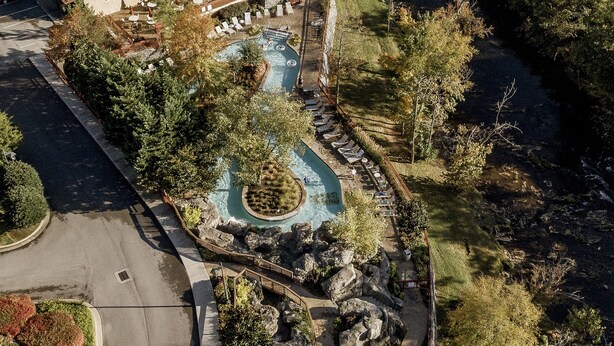 An aerial view of a hotel with a landscaped pool area, outdoor seating, and a parking lot.